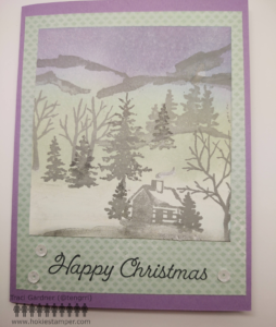 Card with a winter scene showing mountains in the background, trees, and a small cabin, with the sentiment Happy Christmas