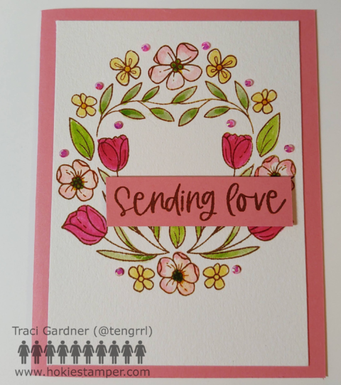 Spring flowers in a wreath on the front of a cream and pink card, with the sentiment, Sending love