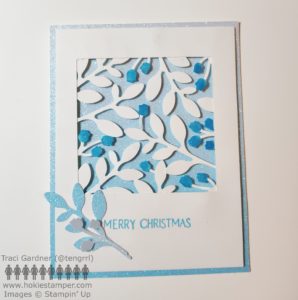 A blue and white card with silhouettes of flowers and leaves in white on a blue glitter paper background with the sentiment Merry Christmas.