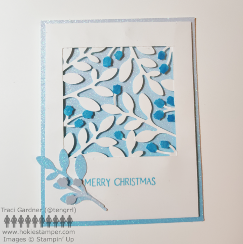 A blue and white card with silhouettes of flowers and leaves in white on a blue glitter paper background with the sentiment Merry Christmas.