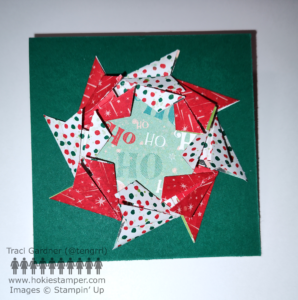 Folded Christmas paper in a round pattern, with a green patterned paper circle in the middle to fake the hole in the center of the wreath. The wreath is mounted on a dark green card base.