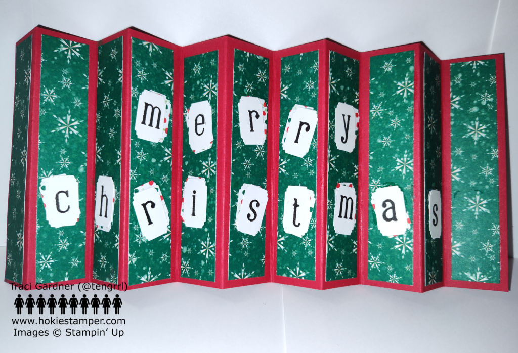 An accordion card with a red background and green patterned paper, showing white snowflakes, and the message Merry Christmas.