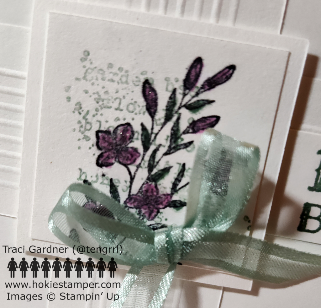 Detail of the floral focal image showing soft green worn text with purple flowers stamped over. A soft green bow is in the lower right corner.