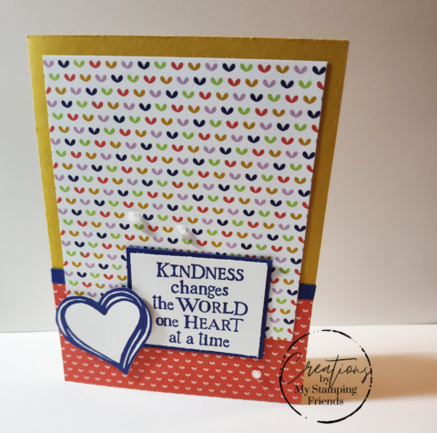 Red and yellow greeting card with patterned paper featuring small hearts in a variety of colors. A large heart is offset over the sentiment panel, which states, Kindness changes the world one heart at a time.